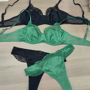 Detailed view of black lace and emerald green satin lingerie sets on a wooden surface