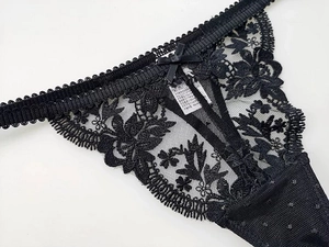 Close-up of black floral lace thong with delicate scalloped edges and a satin bow detail