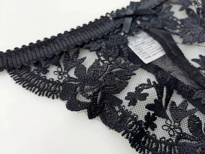 Detail of floral lace embroidery and satin bow on sheer black thong underwear