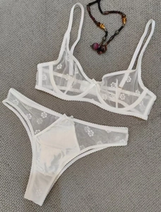 Flat lay of white sheer lace bra and matching thong with floral embroidery and bow details