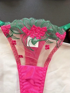 Detail of pink satin lingerie with floral embroidery and green leaf lace accents