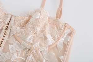 Détail macro du corset en mesh champagne avec broderies florales blanches et dentelle fine
