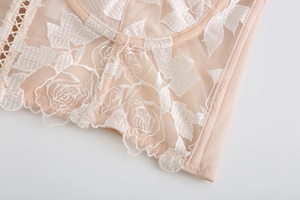 Détail de broderie florale sur corset en dentelle chair avec bords festonnés et maille