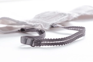 Detail of white lace bra with adjustable grey elastic shoulder strap and silver buckle