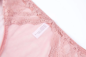 Detailed macro view of pink floral lace fabric and cotton lining with garment care label