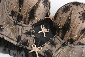 Close-up of black mesh lace bra with gold floral embroidery and pink ribbon bows