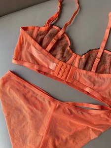 Detail of bright orange lace bra featuring black eyelash trim and breathable mesh texture