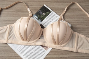 Detailed view of beige lace push-up bra with satin straps and mesh wings on wooden background