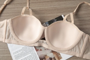 Detail of a beige balconette bra with sheer mesh side wings on a wooden desk