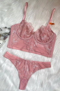 Detail of pink floral lace bustier set with 75B size tag on a soft white plush surface