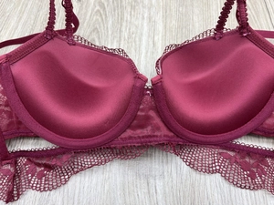 Detail view of burgundy lace bra with underwire support and pleated strap on wooden background