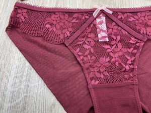 Detail view of burgundy floral lace panties with a small pink bow on a wooden surface