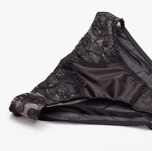Detailed close-up of black floral lace embroidery and satin fabric on the elegant panties