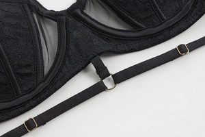 Detail of black lace lingerie showing adjustable gold metal rings and satin strap textures