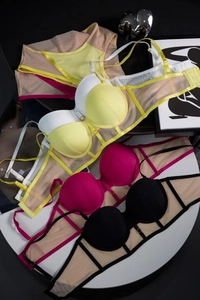 Flat lay of mesh patchwork lingerie sets in yellow, rose, and black on a white tray