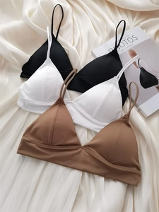 Three seamless triangle bras in black, white, and camel on soft silk fabric background