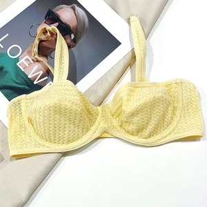 Close-up of light yellow lace bra featuring honeycomb mesh texture and gold metal buckles