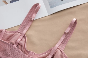 Detail of light pink lace bra strap with metal buckle on breathable mesh fabric