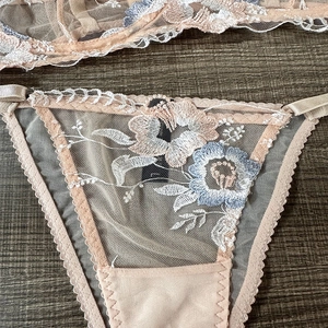 Détail de la lingerie en maille abricot avec broderies florales bleues et blanches
