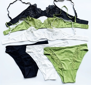 Flat lay view of three lace lingerie sets in black, white, and green on white background