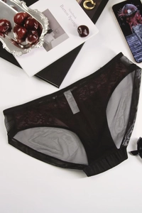 Detailed view of black lace and mesh panties with intricate floral patterns on a white desk