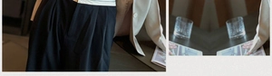Détail d'un blazer blanc ajusté associé à un pantalon noir plissé à taille haute
