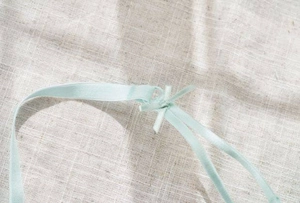 Detail of light green silk ribbon with a bow on natural linen fabric background