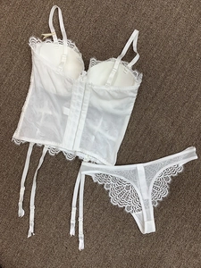 Body en dentelle blanche avec porte-jarretelles et string assorti posés sur un tapis