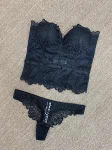 Ensemble lingerie en dentelle noire avec bustier push-up et string assorti posé sur un tapis
