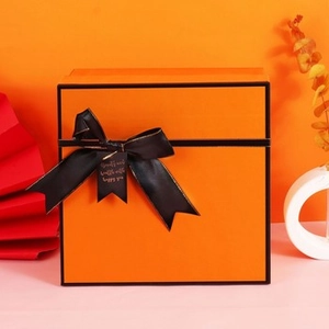 Macro detail of luxury orange gift box featuring a black satin bow and golden message tag