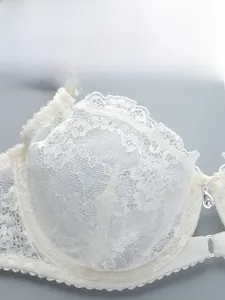 Close-up of white floral lace bra cup with scalloped edges and crystal bow pendant detail