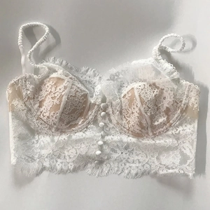 Detail of white eyelash lace bra with fine straps and button accents in a vintage style
