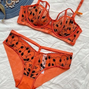 Set lingerie in pizzo arancione con reggiseno a rete e slip trasparenti su sfondo bianco
