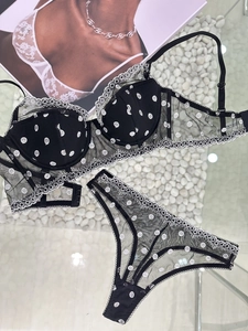 Detail of sheer black polka dot mesh bra with delicate white lace trim on pebbles