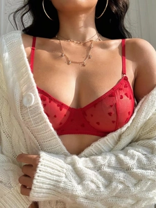 Detail of red mesh bra with heart print under a white cardigan with gold accessories