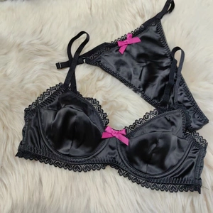 Detail of black satin lingerie set with heart lace trim and pink bows on white fur background