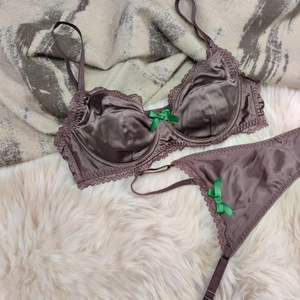 Detail of satin bra and panty set with lace trim and green ribbon bow on plush carpet