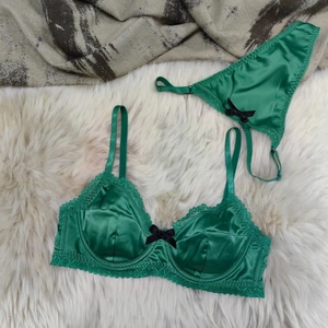 Flat lay of emerald green satin and lace lingerie set with bow details on fur texture