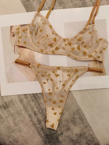 Flat lay detail of mesh heart print lingerie set with bra and thong on a beige background