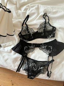 Detailed view of black lace lingerie set with white floral embroidery on a white bed