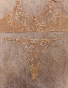 Detail of sheer lace lingerie set featuring sun and moon embroidery on beige mesh fabric