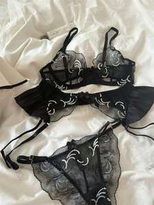 Close-up of black sheer mesh bra with intricate white wave embroidery and garter belt
