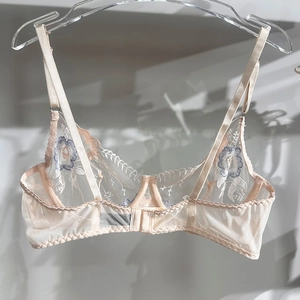 Detail of peach lace bra featuring intricate blue floral embroidery and sheer mesh cups