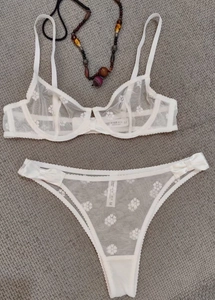Detail of white sheer mesh bra and thong with floral embroidery and satin bows