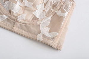 Detailed close-up of French rose floral embroidery on beige lace bra with mesh texture