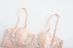 Detail of pink lace bra featuring white rose embroidery and elegant cross-strap center