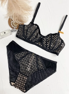 Lace lingerie set with sheer mesh detailing and gold buckles on a white textured backdrop