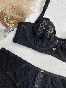 Detail view of black lace bra and panty set with elegant gold buckle on white texture