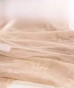 Close-up of beige lace mesh fabric with intricate floral embroidery and sheer texture