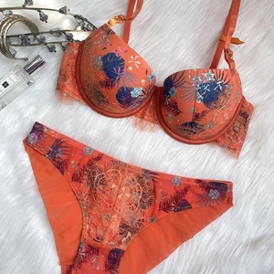 Detailed close-up of coral orange lace lingerie set with tropical print on white plush rug